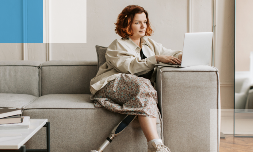 A lady with a prosthetic leg, sat on a sofa, using a laptop